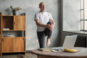 man doing yoga exercise at home using online lesson on notebook