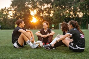young people sit on grass in a semi circle as the sun sets behind them