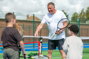 a tennis coach teaches two young people how to play the sport