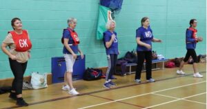 people line up in a sports hall to practice walking netball